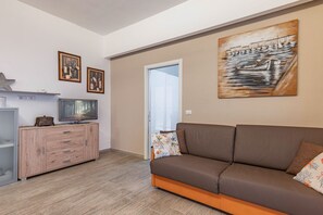 A living room with a sofa, a TV on a wooden cabinet, and artwork on the walls. - GuestHost - Cozy apartment of about 45 sqm, for 4 people, on the ground floor of a three-story building (a few steps to access). The property, just 50 meters from the sea, is located in Schisò, a hamlet of Giardini Naxos, a seaside area full of points o (Giardini Naxos)