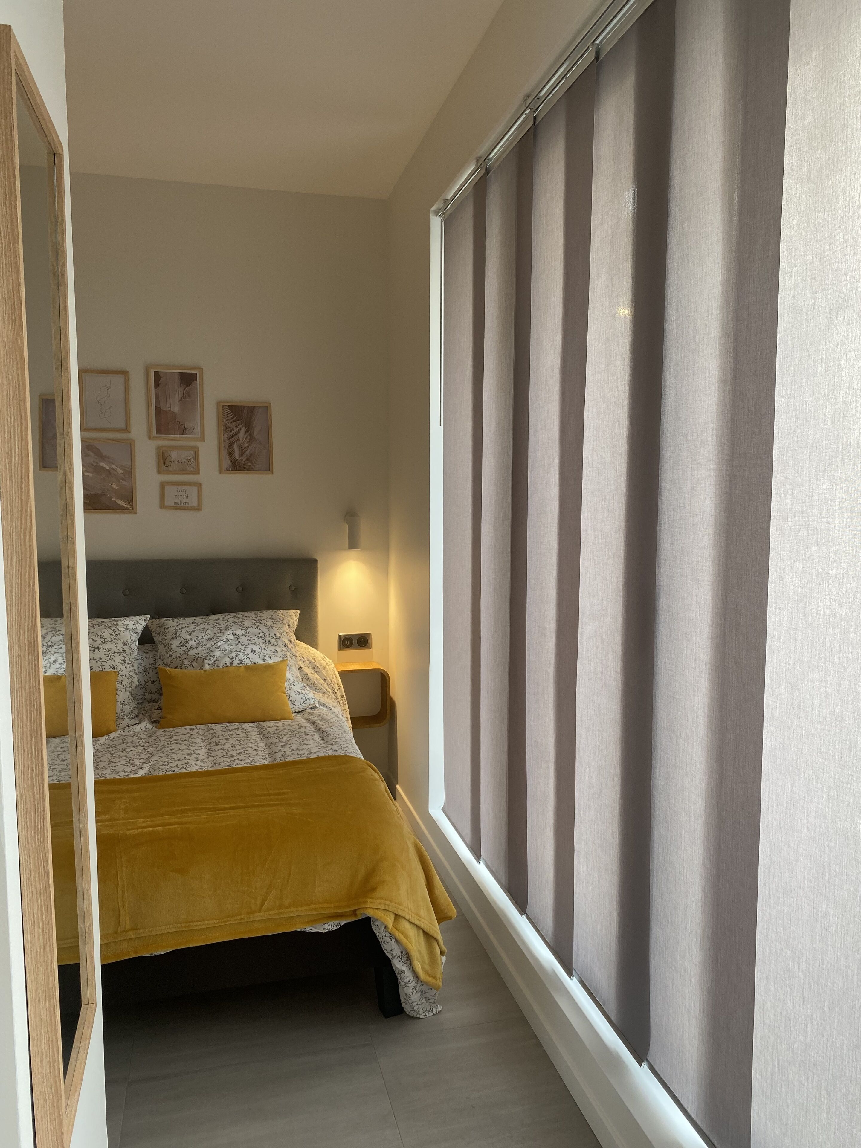 A bedroom with a bed, a nightstand, a wall-mounted lamp, and framed artwork.