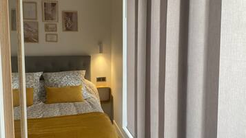 A bedroom with a bed, a nightstand, a wall-mounted lamp, and framed artwork.