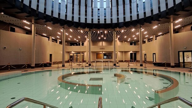 A large indoor swimming pool with a central island, surrounded by a spacious area with multiple doors and a high ceiling with a skylight. - Studio 2 minutes from the NANCY THERMAL complex (Nancy)
