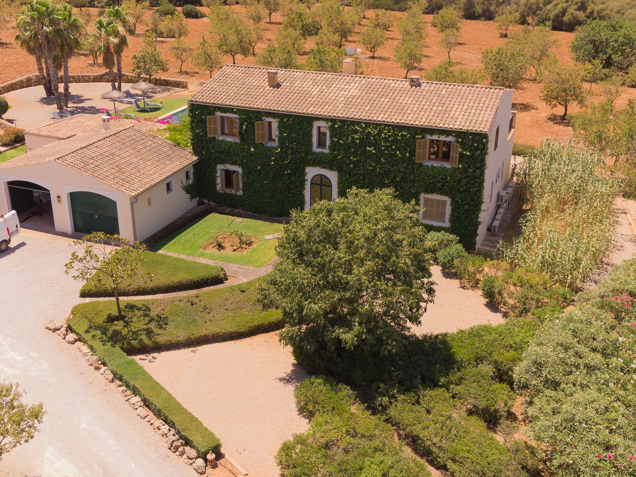 A large house with a tiled roof, surrounded by a well-maintained garden and a driveway.