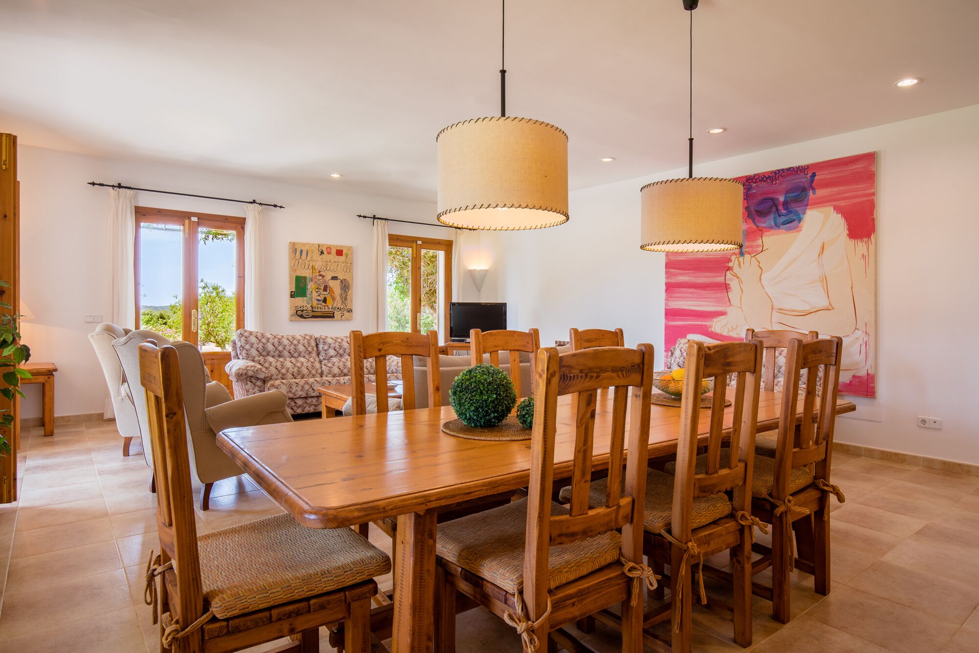 A dining area with a wooden table and chairs, a sofa, and a painting on the wall.