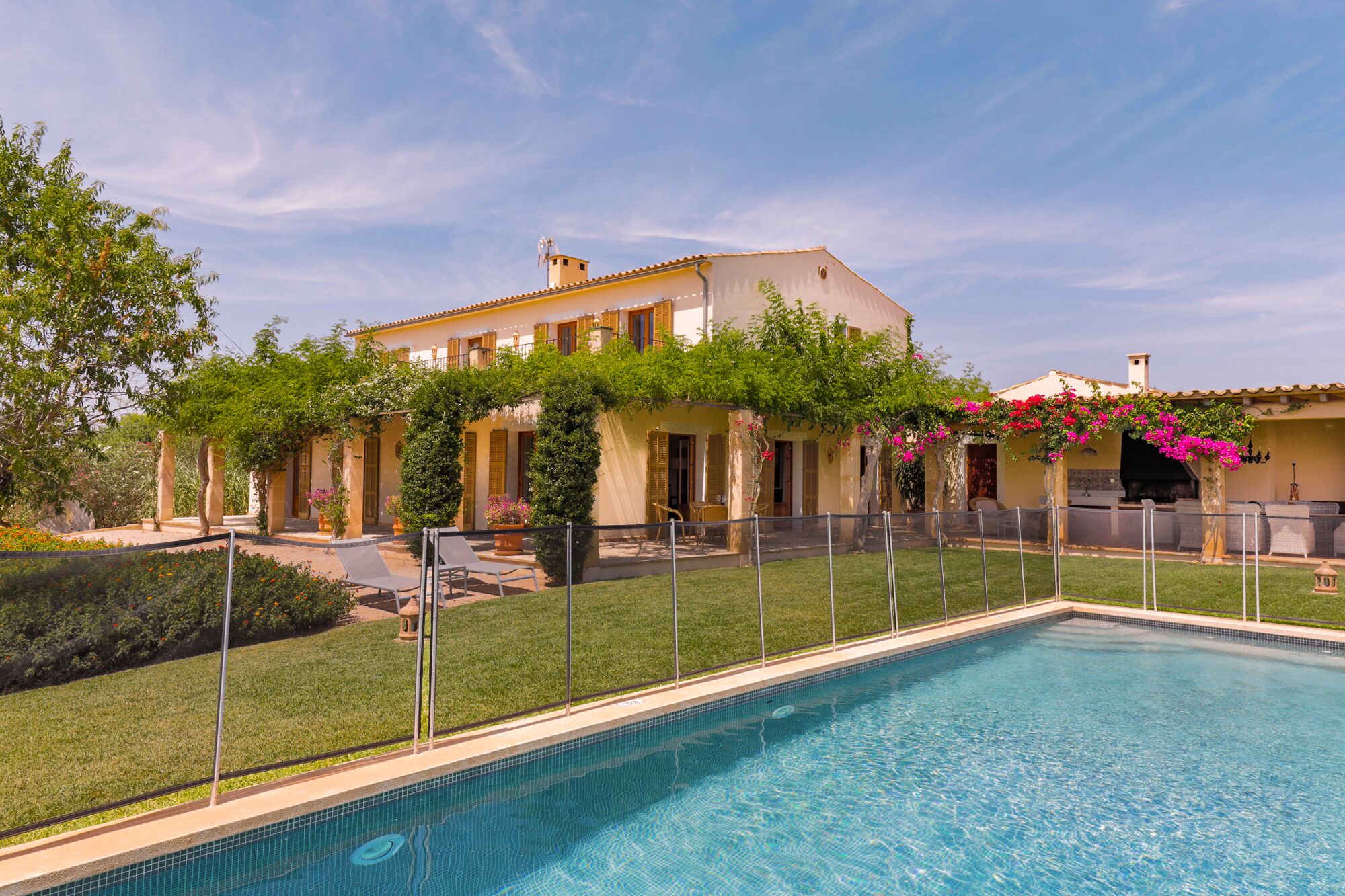 A poolside view of a Mediterranean-style villa with a swimming pool, outdoor seating, and lush greenery.