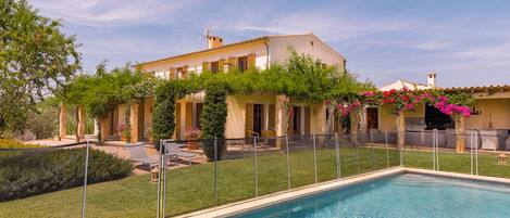 A poolside view of a Mediterranean-style villa with a swimming pool, outdoor seating, and lush greenery.