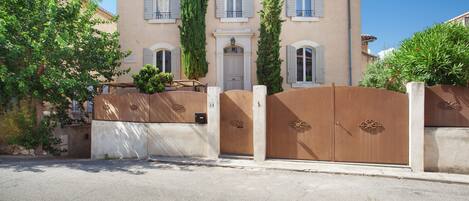 Un edificio de dos plantas con fachada color beige, una entrada central con puerta y un camino de acceso con portón.