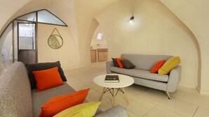 Una sala moderna con un sofá gris, cojines naranja y amarillos, una mesa de centro blanca y un gran techo abovedado.