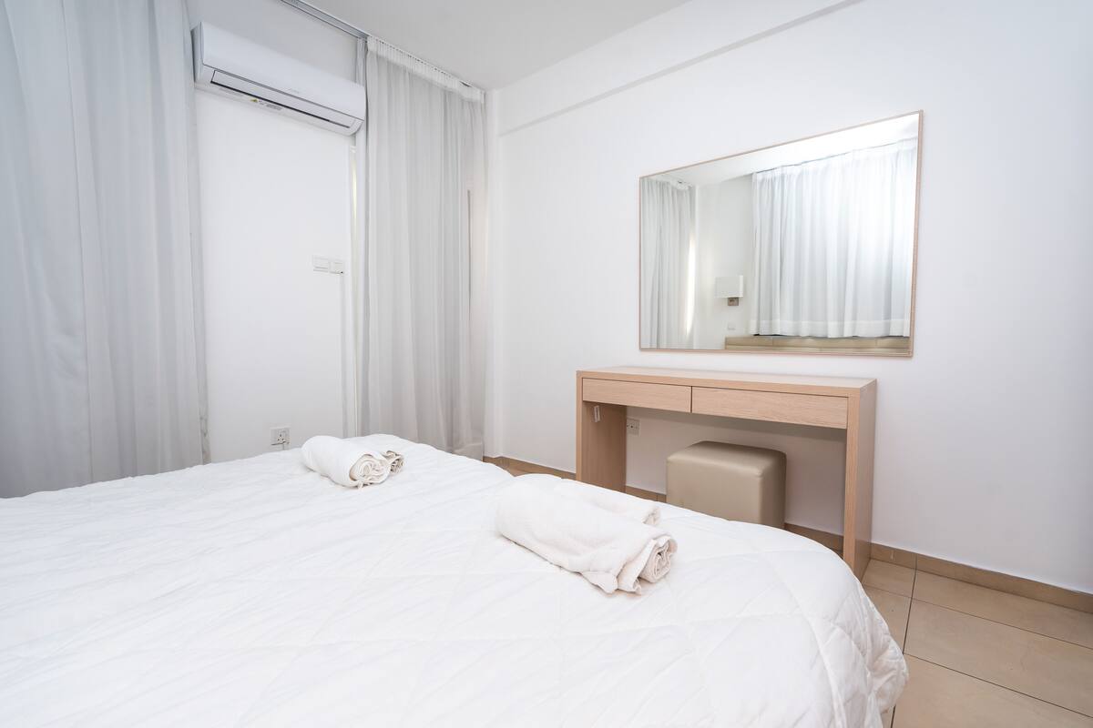 Una habitación de hotel con una cama, una mesita de noche, un espejo y un equipo de aire acondicionado.