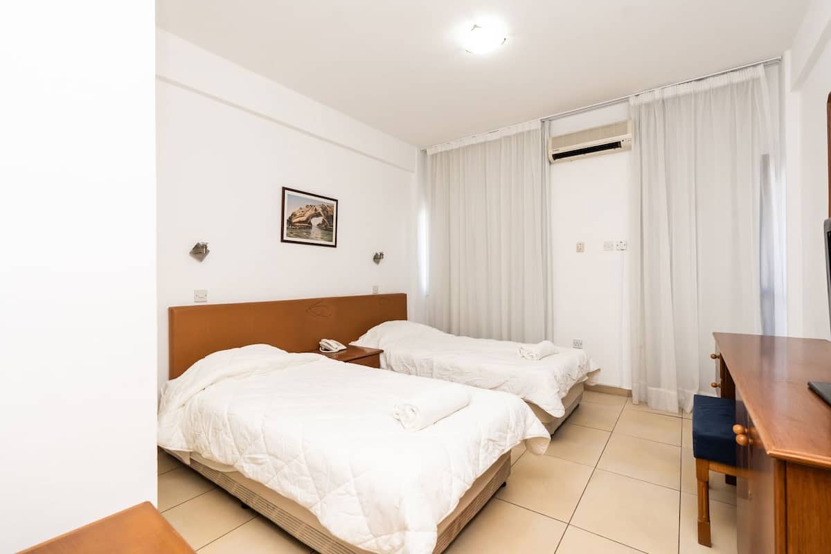Habitación de hotel con dos camas, un escritorio, un teléfono y un cuadro en la pared.
