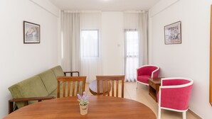 Uma sala de jantar com mesa de madeira, sofá verde e duas cadeiras vermelhas.