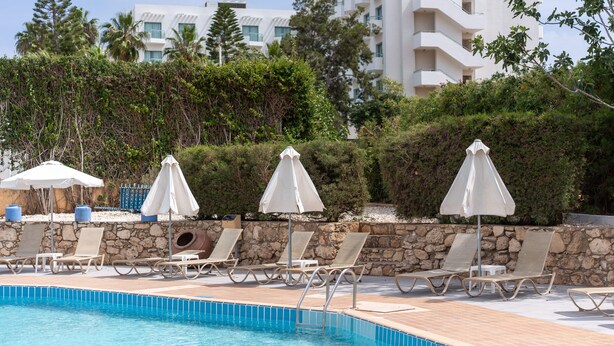Uma piscina com espreguiçadeiras e guarda-sóis, cercada por um muro de pedra e vegetação.