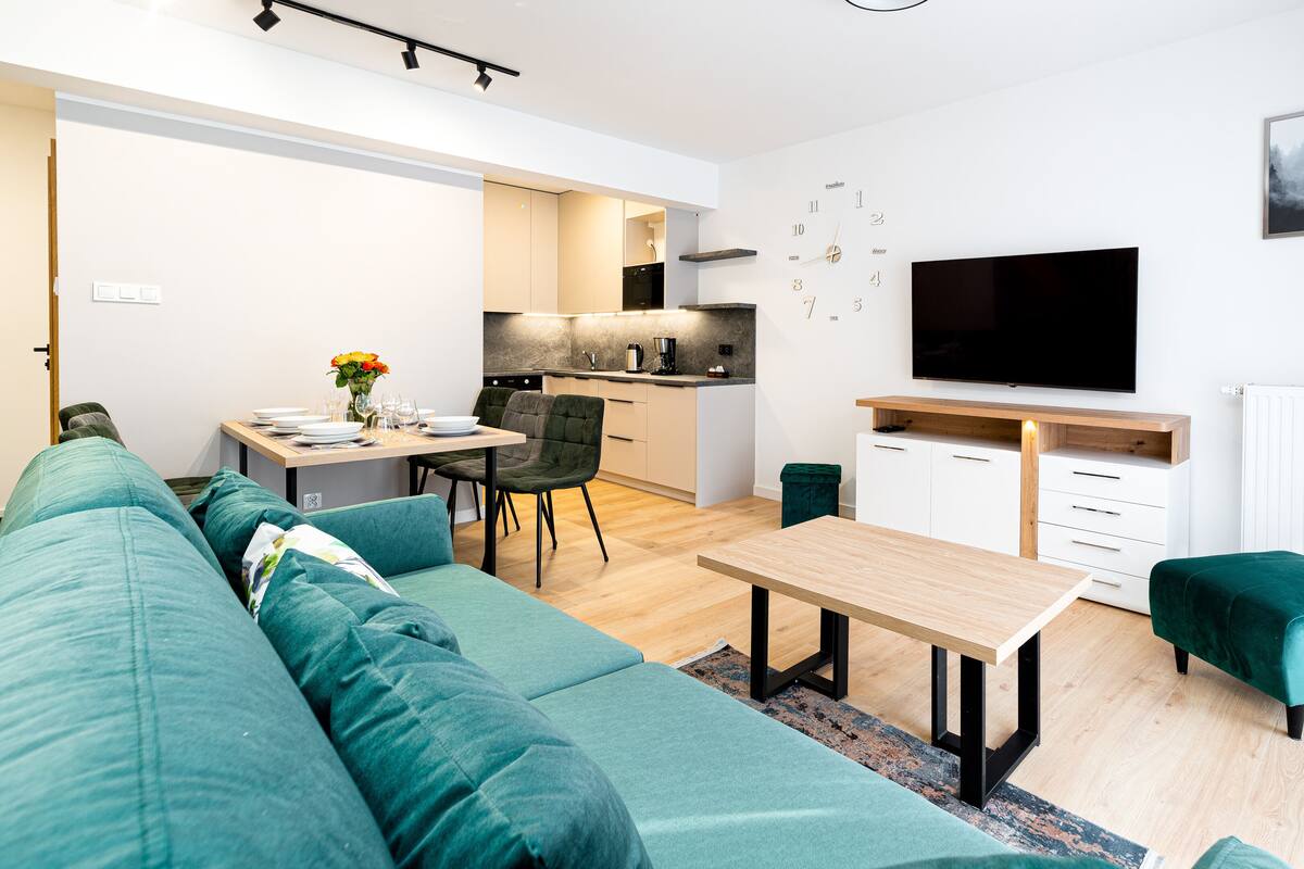 Una sala de estar moderna con un sofá, una mesa de centro y un televisor. Cuenta con una zona de cocina con una mesa de comedor y sillas.