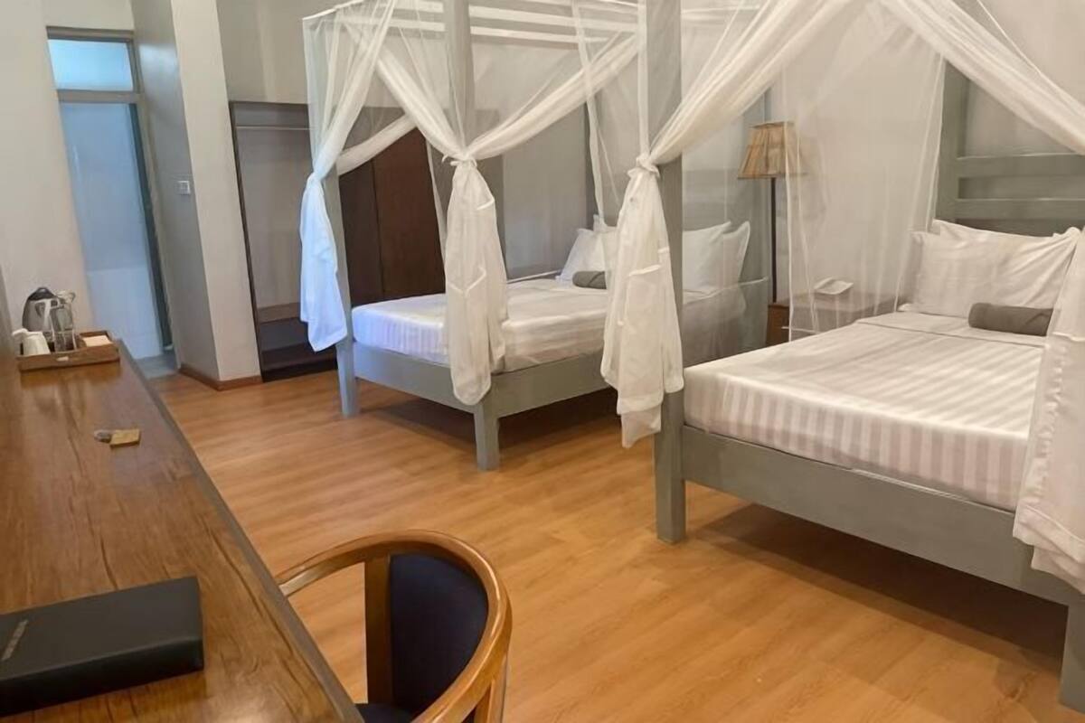 A room with two beds, a wooden desk, and a chair.