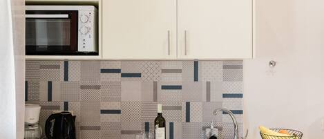 A kitchen with a microwave, coffee maker, wine bottle, glasses, and a fruit bowl.