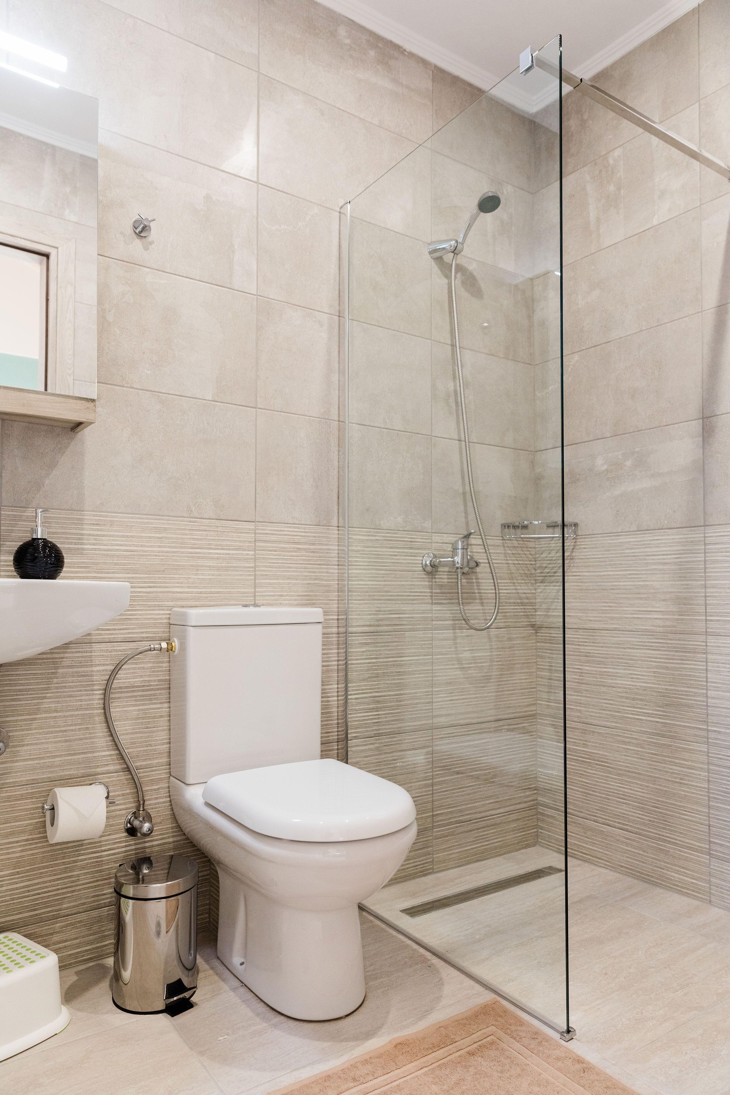 A modern bathroom with a glass-enclosed shower, a toilet, and a sink with a soap dish.