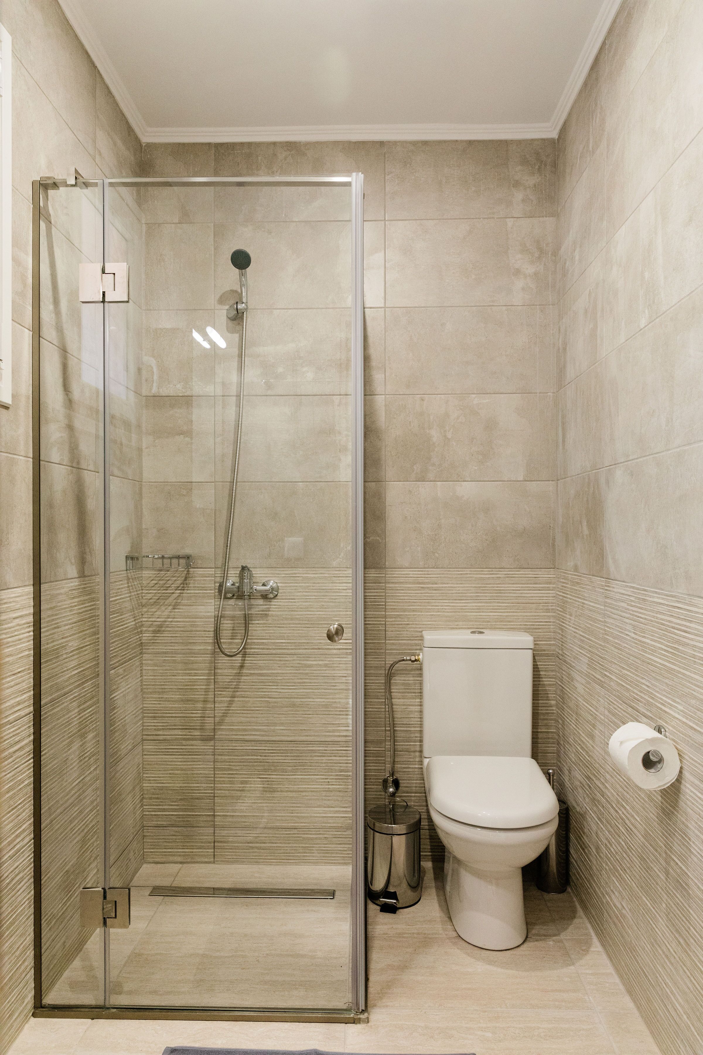 A modern bathroom with a glass-enclosed shower, a toilet, and a trash bin.