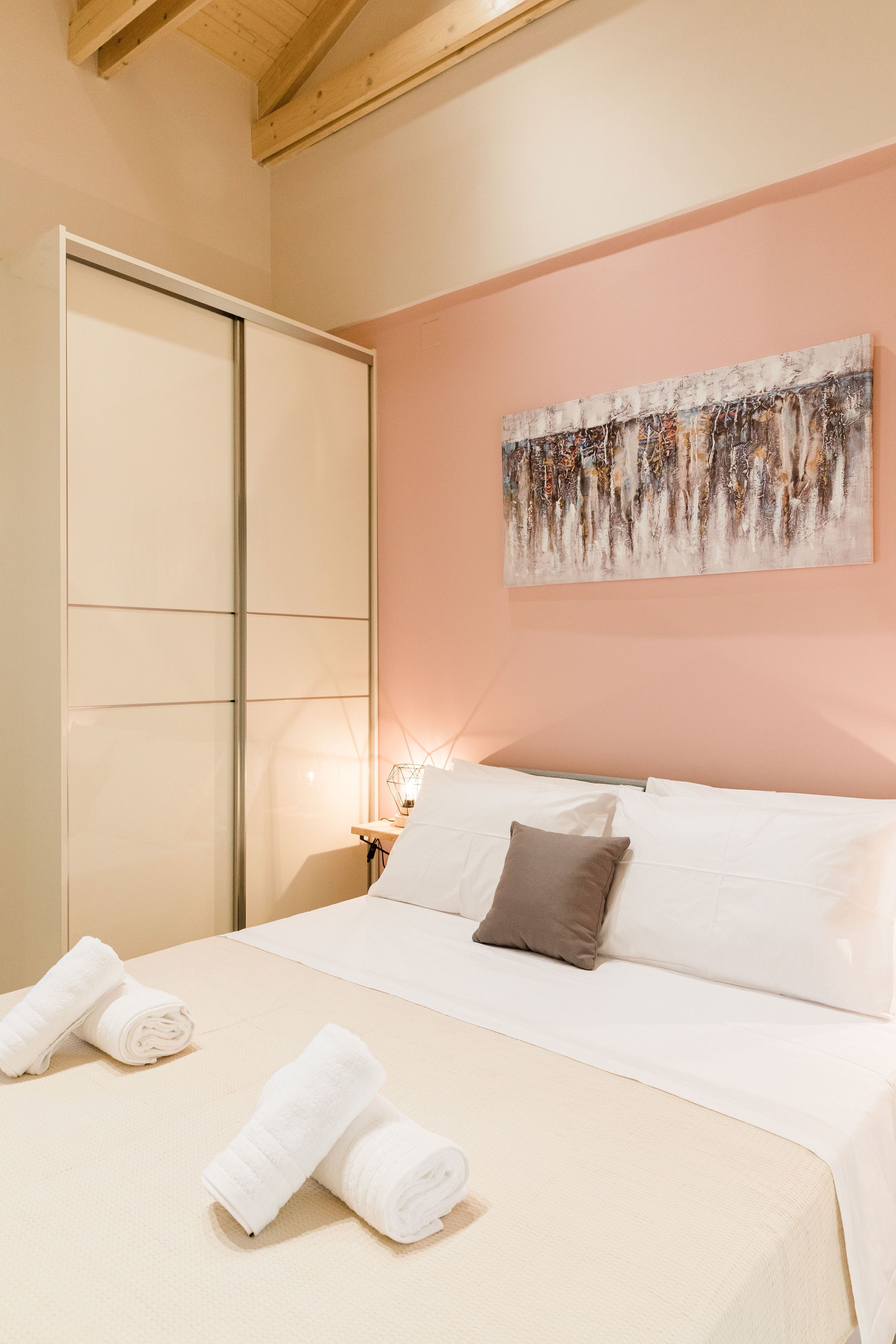 A bedroom with a bed, pillows, a painting on the wall, and towels on the bed.