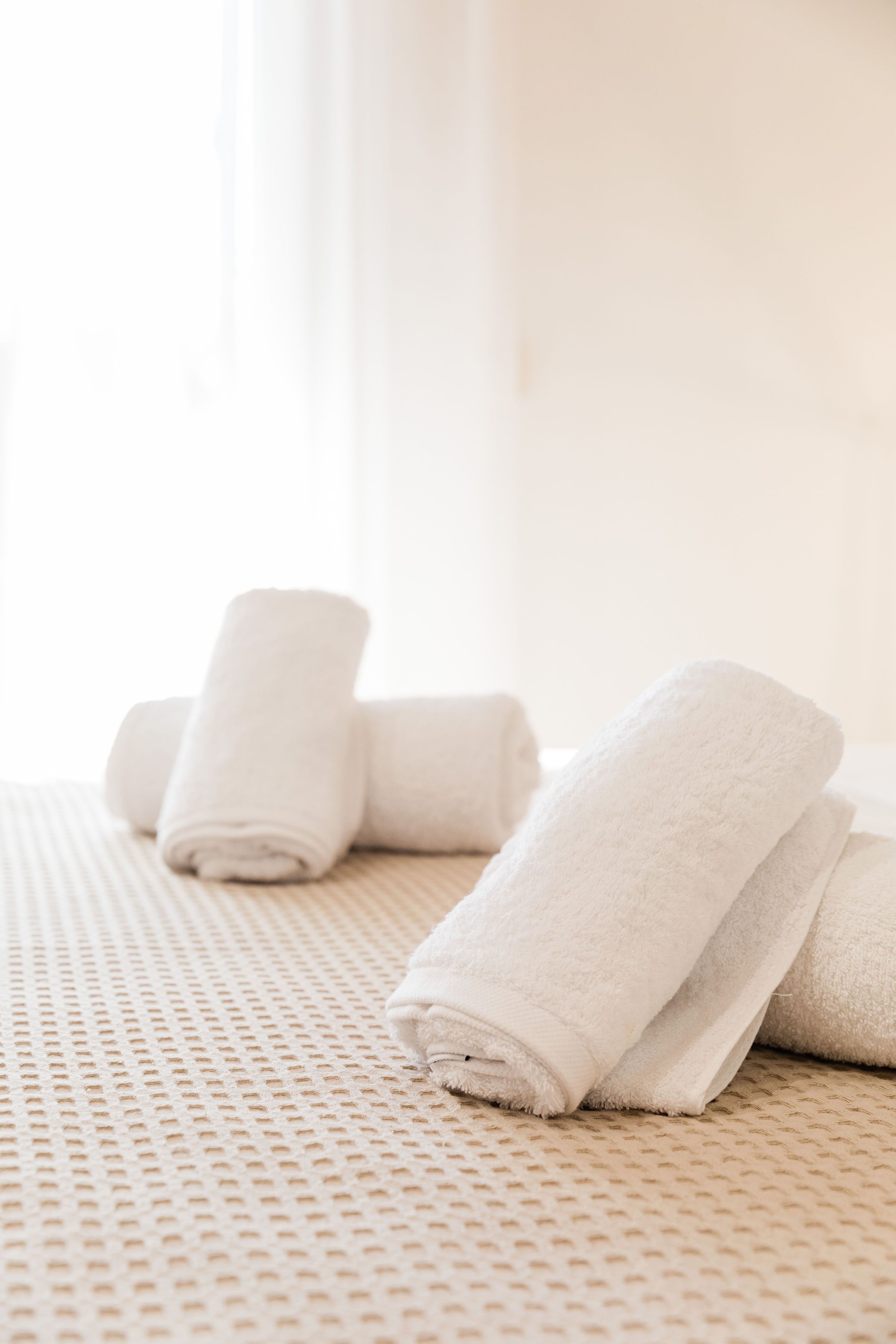 Sauber gefaltete weiße Handtücher auf einer strukturierten beigefarbenen Bettdecke in einem hellen Zimmer.