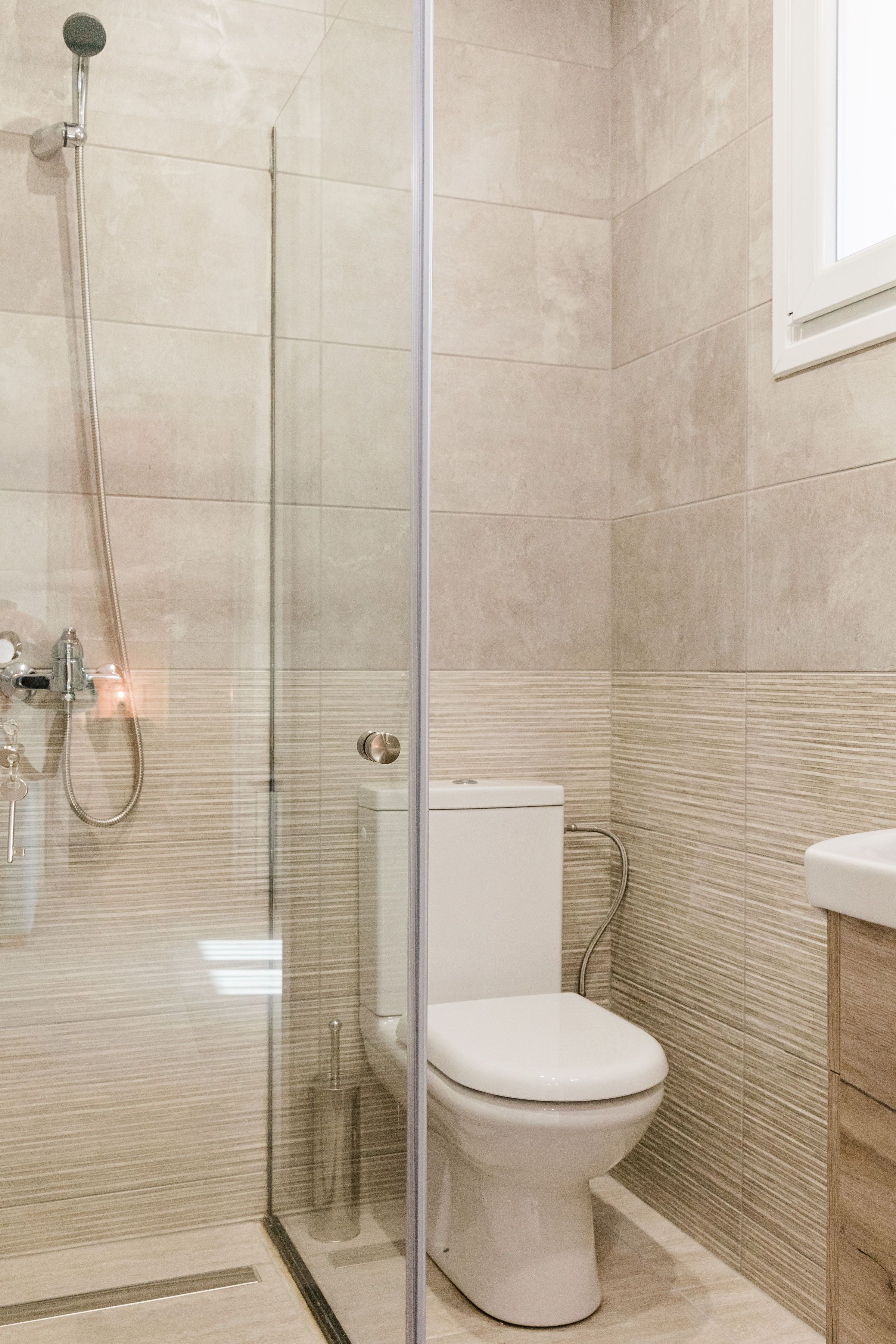 A modern bathroom with a glass shower enclosure, a white toilet, and beige tiled walls.