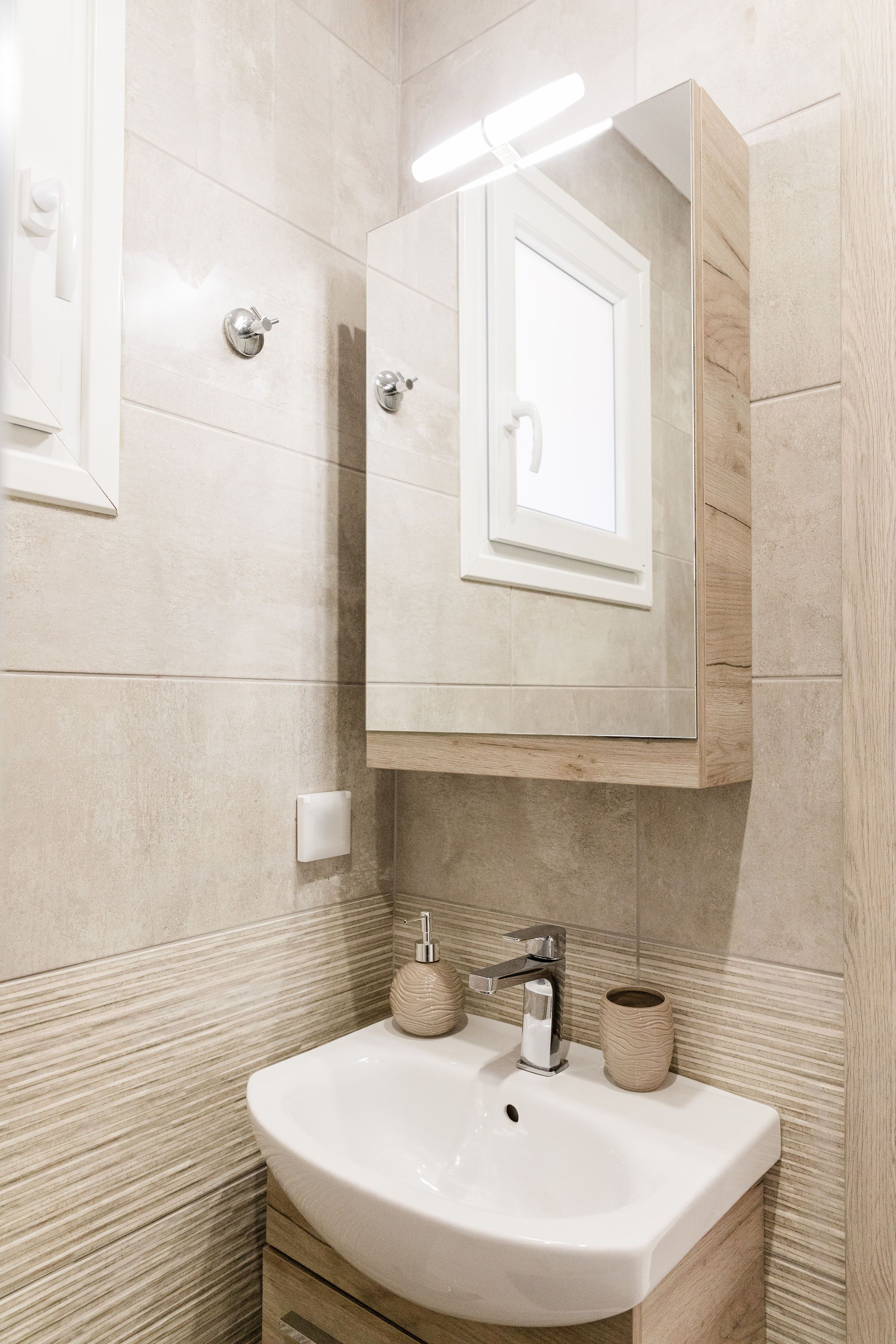 A bathroom with a white sink, a mirror, and a light fixture above the mirror.