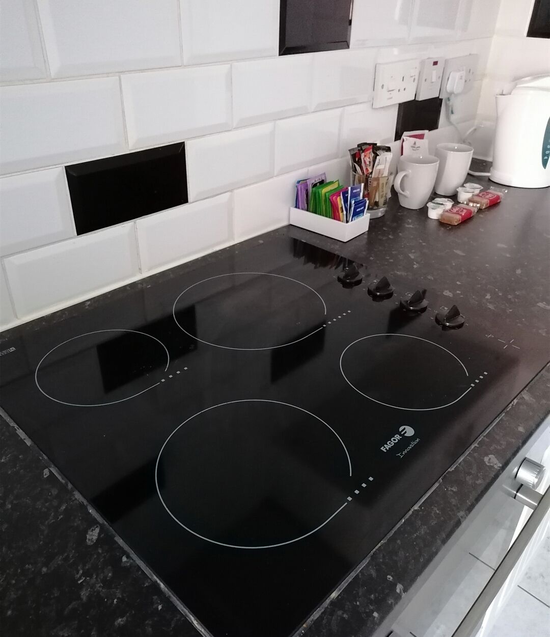 Une cuisine dotée d’une plaque de cuisson à induction noire, d’un crédence carrelée blanche et d’une machine à café posée sur le plan de travail.