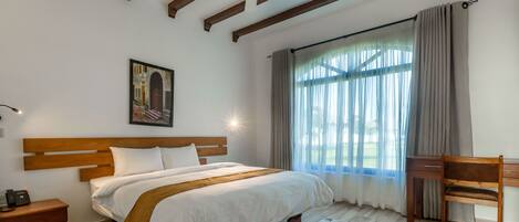 A bedroom with a wooden bed, a desk, a chair, a large window with curtains, and a ceiling fan.