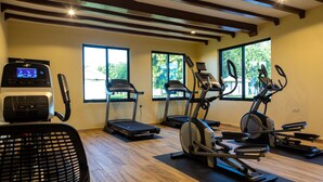Un gimnasio con cintas de correr, elíptica y bicicleta estática, amplias ventanas y suelos de madera.