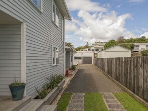 A residential driveway leading to a house with a wooden fence and a garage. - The Beach House - Kuaotunu Holiday Unit (Kuaotunu)