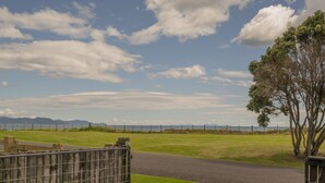 A paved pathway leading to a fenced area with a grassy field and a tree.