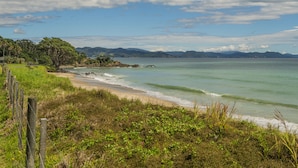 A coastal landscape with a beach, grassy areas, and a wooden fence.