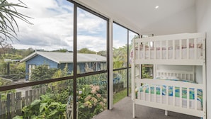A room with a bunk bed, large windows, and a view of a garden and neighboring houses.