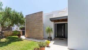 Une maison moderne avec un mur en pierre, une cour verdoyante et des plantes en pot.