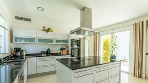 Une cuisine moderne avec des meubles blancs, un plan de travail noir, des appareils en acier inoxydable et une grande fenêtre agrémentée de rideaux.