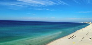 Uma praia com águas claras, uma orla arenosa e a silhueta distante de uma cidade.