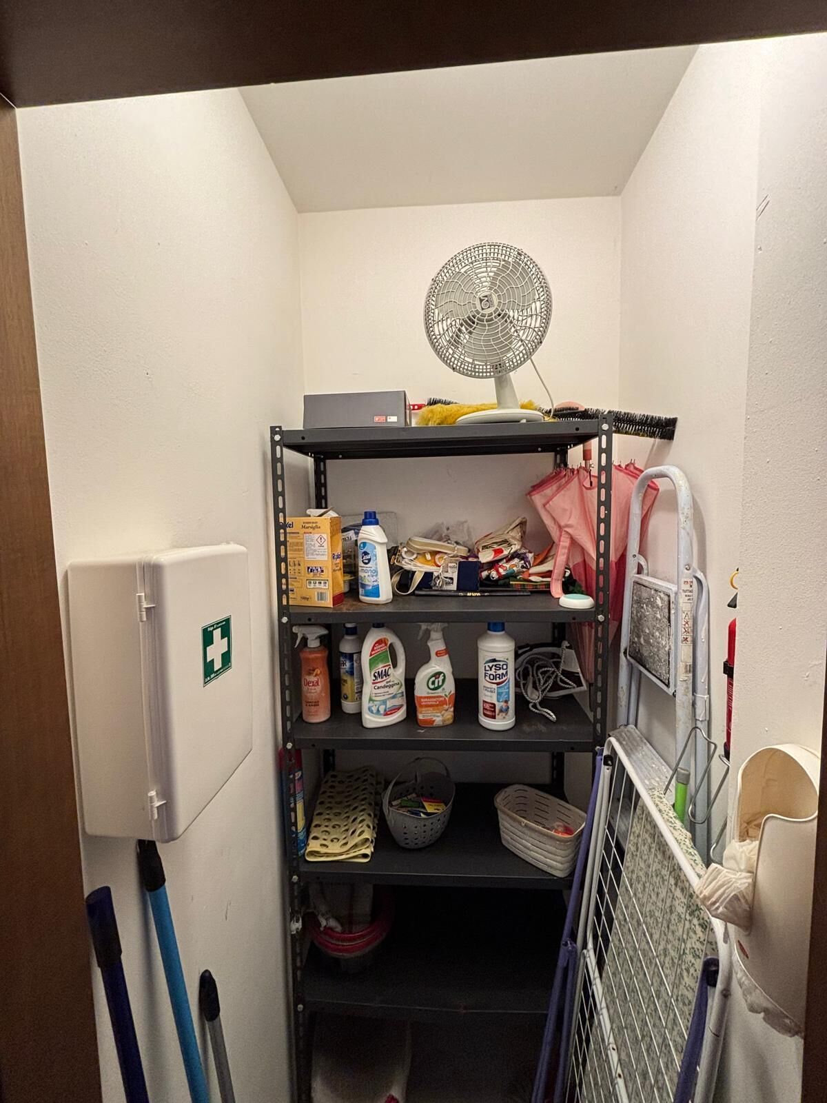 A storage area with shelves containing cleaning supplies, a fan, and a first aid kit.