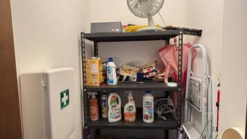 A storage area with shelves containing cleaning supplies, a fan, and a first aid kit.