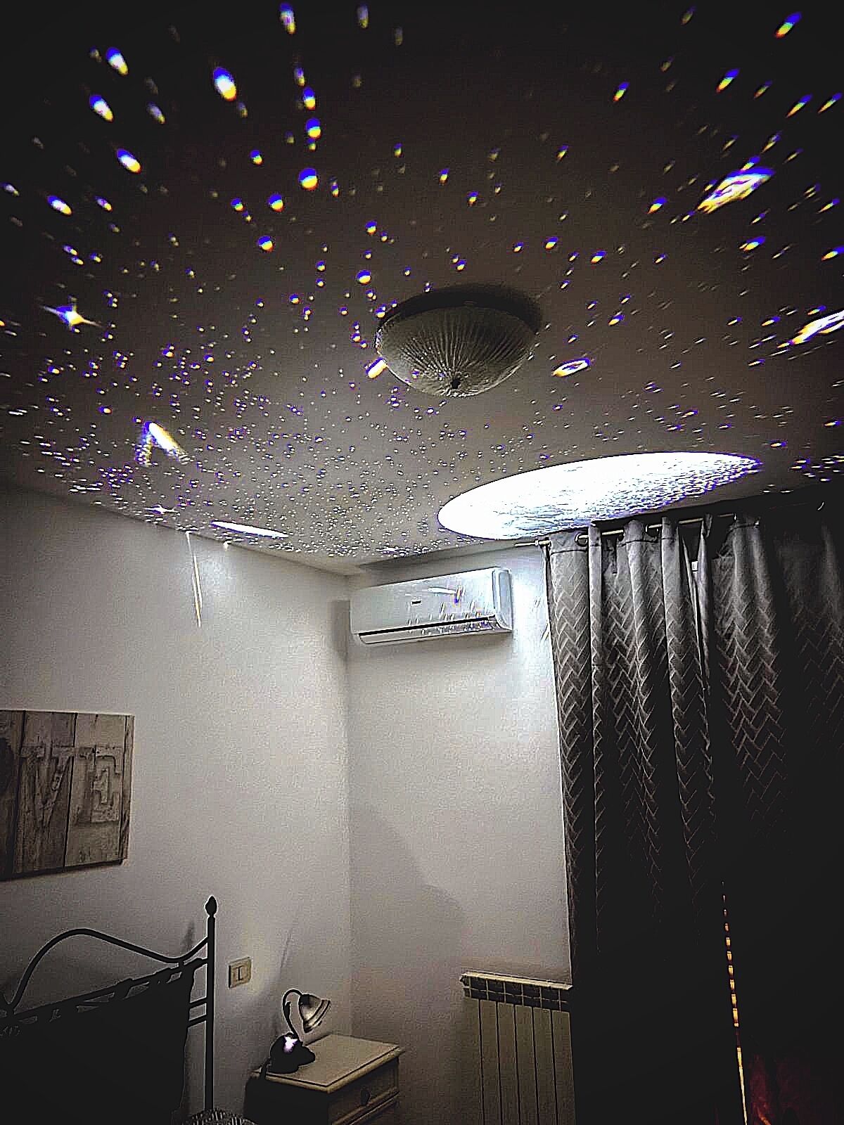 Een kamer met een bed, een radiator, een airconditioning en een plafond met een bijzondere lamp.