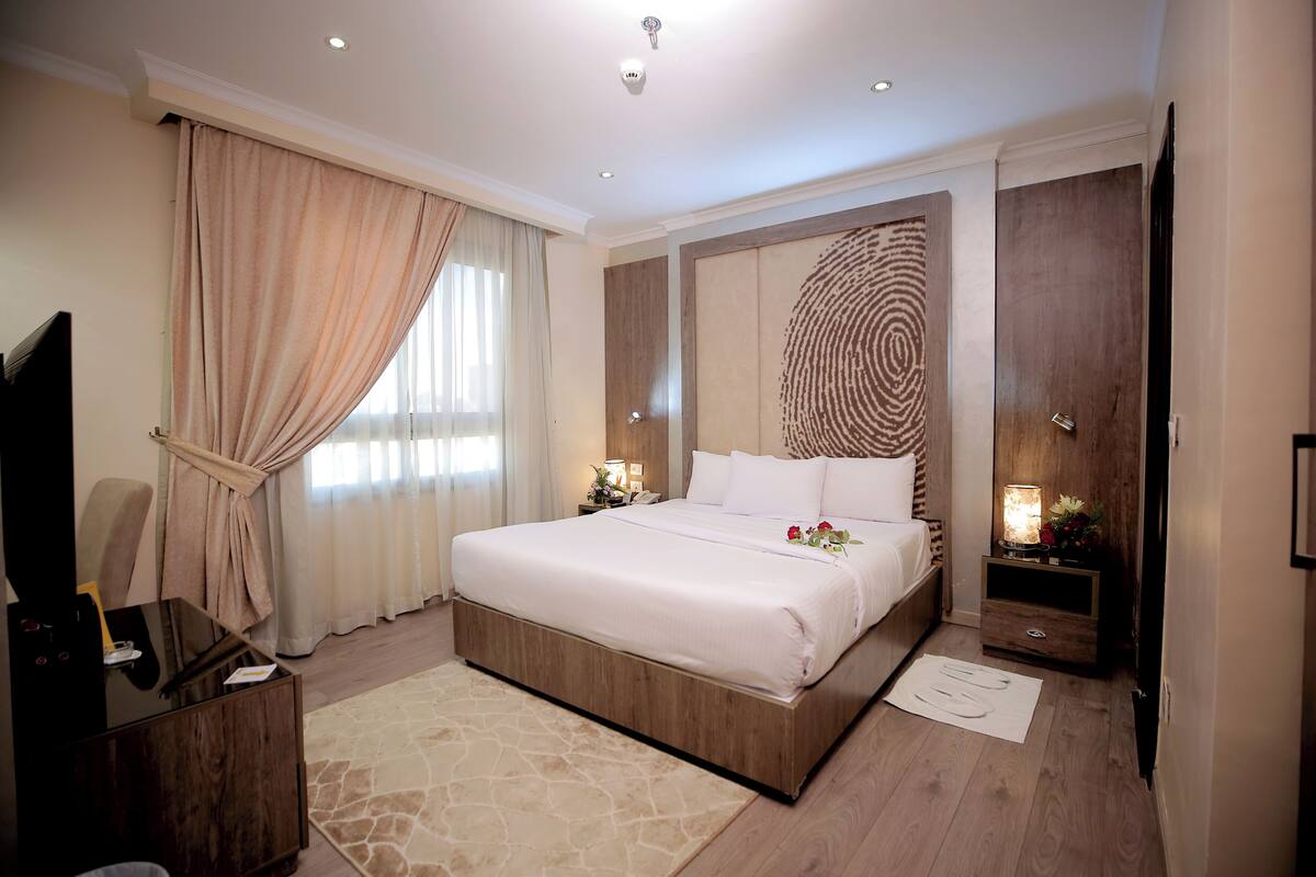 A bedroom with a large bed, a wooden headboard, a nightstand with a lamp, and a TV on a stand.