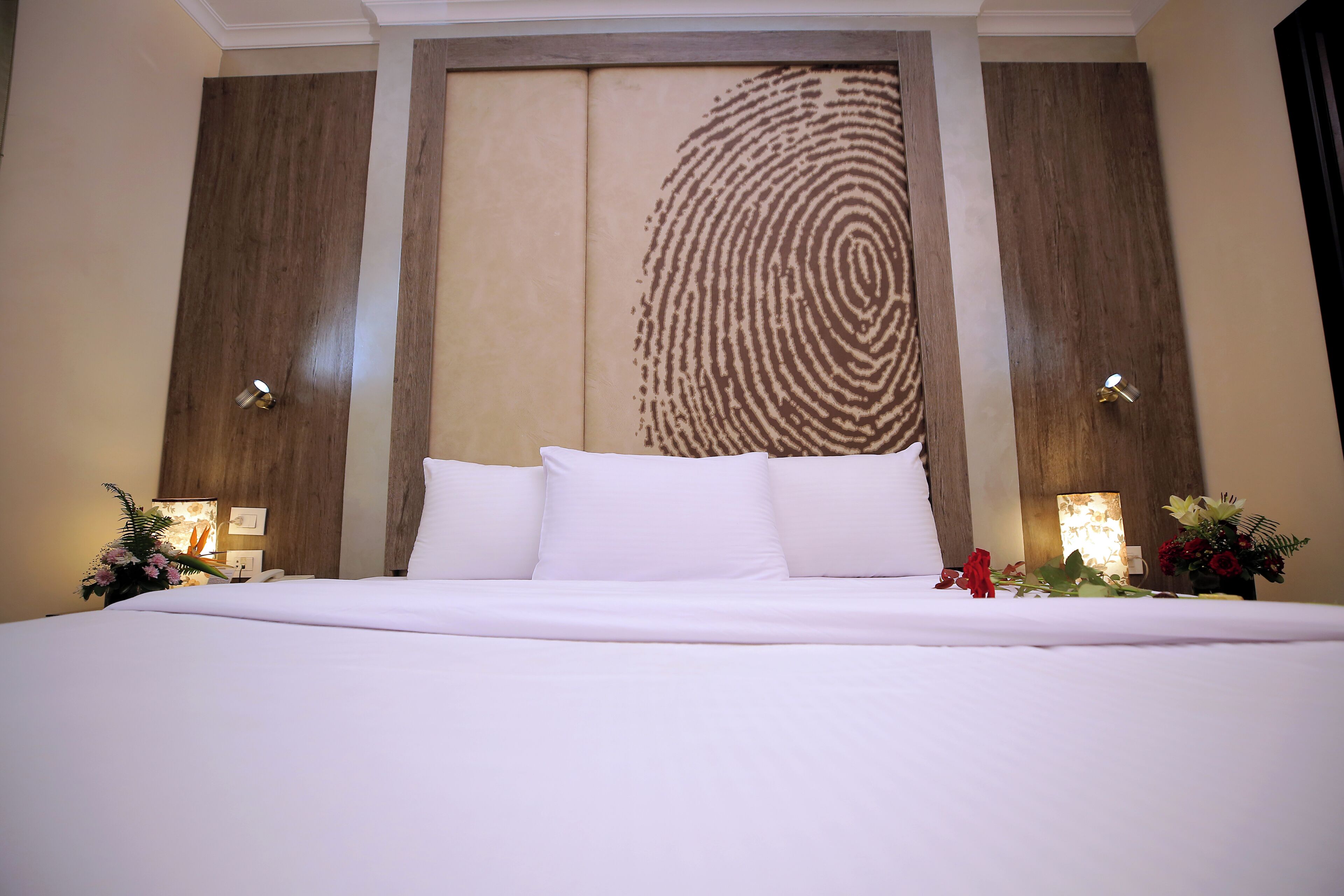 A large bed with white linens, a wall-mounted fingerprint design, and two bedside lamps.
