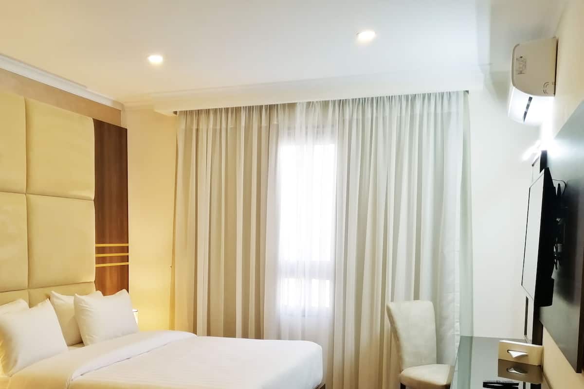 A hotel room with a large bed, a bedside table, a chair, a TV, and a window with curtains.