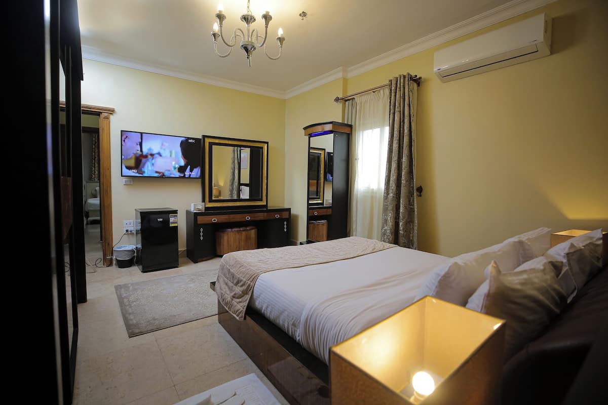 A hotel room with a large bed, a TV, a mirror, and a desk with a computer.