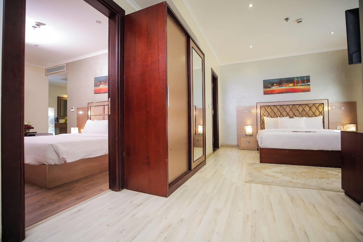A hotel room with a large bed, a smaller bed, a wooden wardrobe, a mirror, and a painting on the wall.