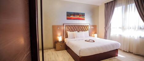 A neatly made bed with a headboard, two bedside lamps, and a painting above it.