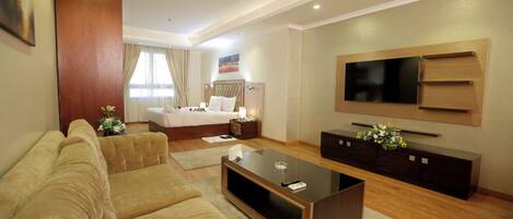 A modern hotel room with a sofa, a coffee table, a TV, and a bed.