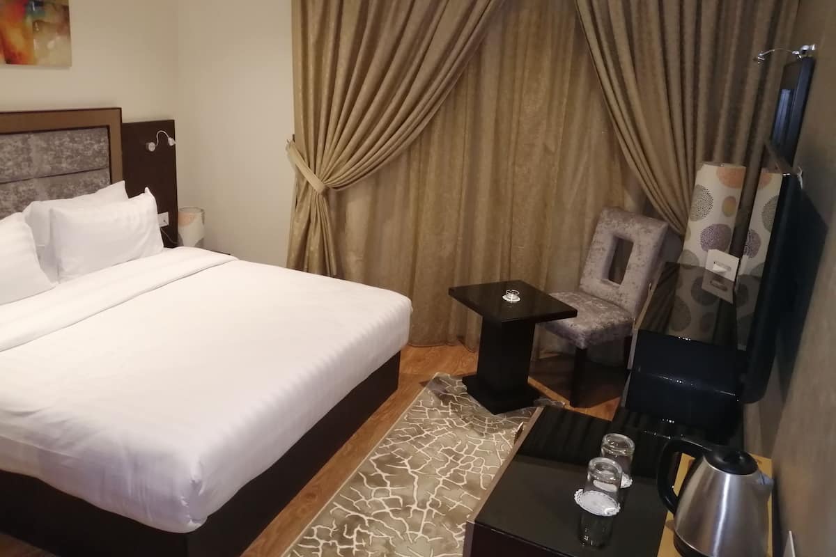 A hotel room with a large bed, a small table with a kettle and glasses, a chair, and a mirror.