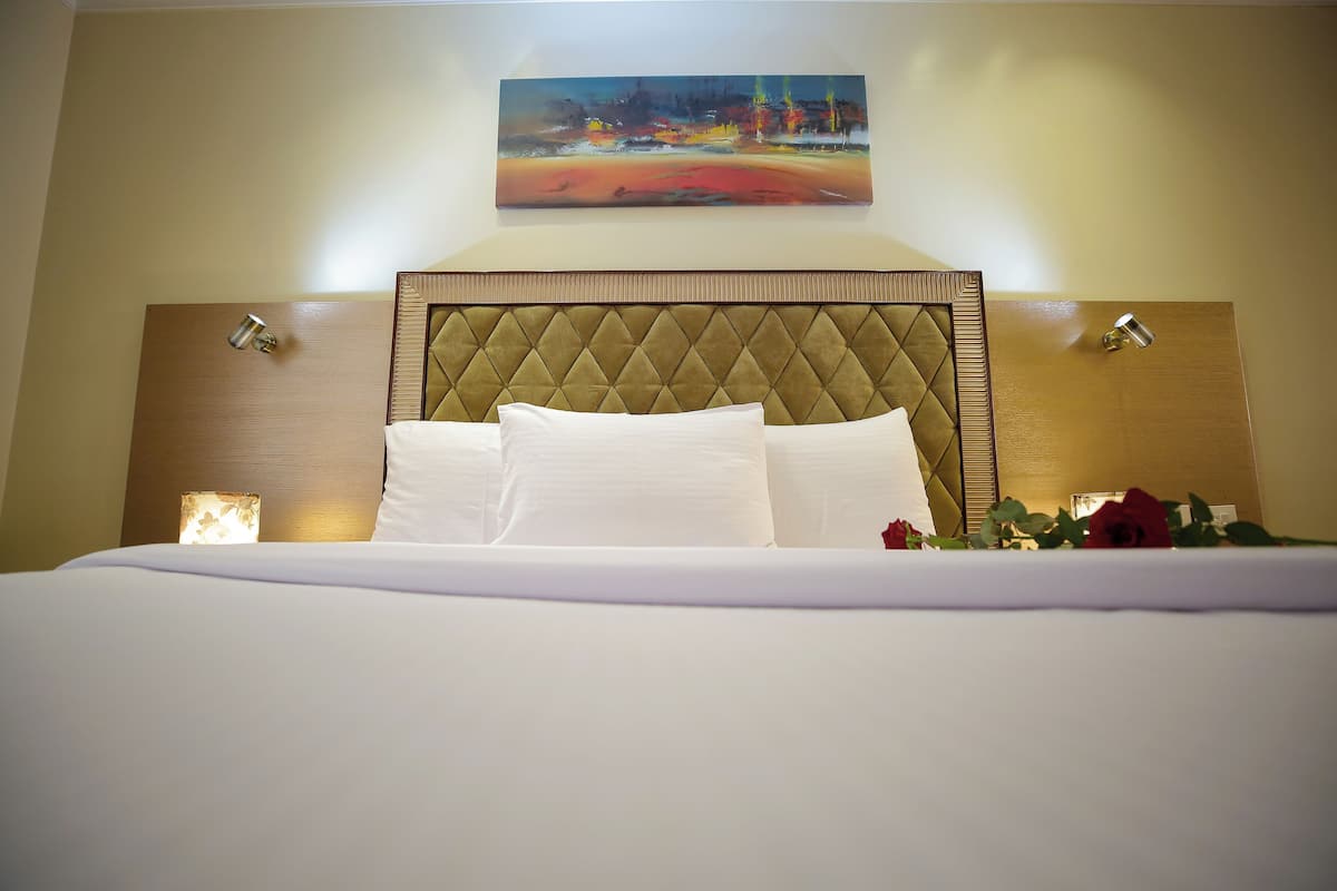 A neatly made bed with a tufted headboard, a painting above, and two wall-mounted lamps.