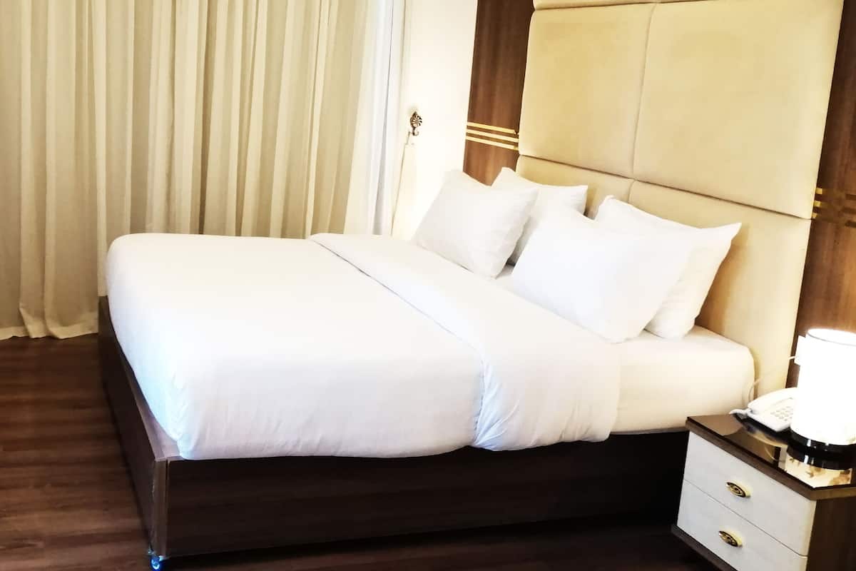A hotel room with a large bed, a wooden headboard, a nightstand with a lamp, and a window with curtains.
