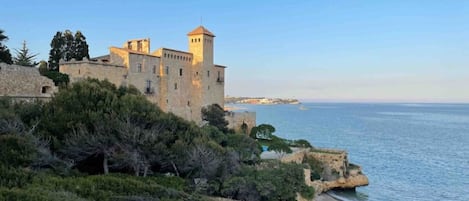 A coastal castle with a tower, surrounded by greenery and overlooking the sea.