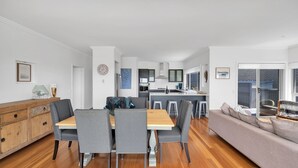 A modern kitchen with dark cabinets, a central island, and a dining area with a wooden table and grey upholstered chairs. - Sapphire on Wilson, Gerringong (Gerringong)