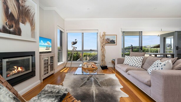 A spacious living room with a fireplace, a large window offering a view of the outdoors, a comfortable sofa, and a coffee table. - Sapphire on Wilson, Gerringong (Gerringong)