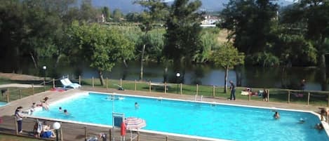 A rectangular swimming pool with a wooden deck and a slide, surrounded by trees and a view of hills.